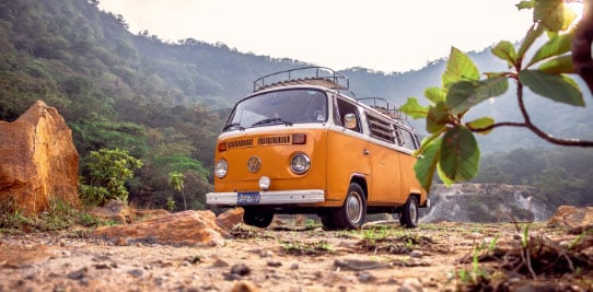 An antique orange VW bus in a mountainous setting
